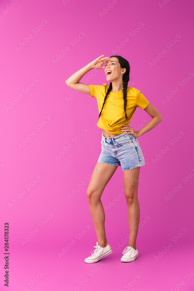 Full length photo of young pleased woman wearing denim shorts looking upward at copyspace with hand at forehead Full length photo of young pleased woman wearing denim shorts looking upward at copyspace with hand at forehead