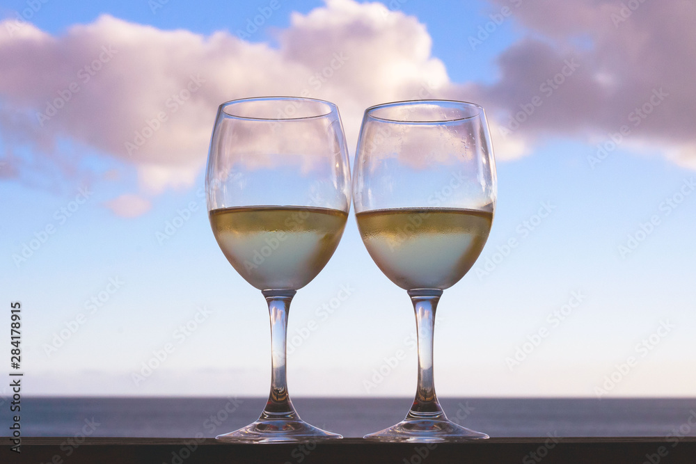Two glasses of white wine on a background of sky and sea. Romantic dinner for two by the sea. Summer evening. Two glasses of white wine on a background of sky and sea. Romantic dinner for two by the sea. Summer evening.