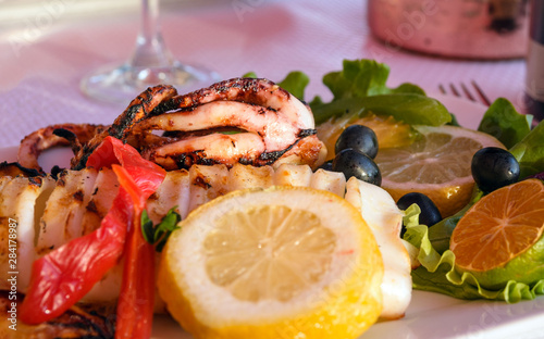 Grilled squid, lemon, olives and wine. Romantic dinner for two by the sea. Warm summer evening.