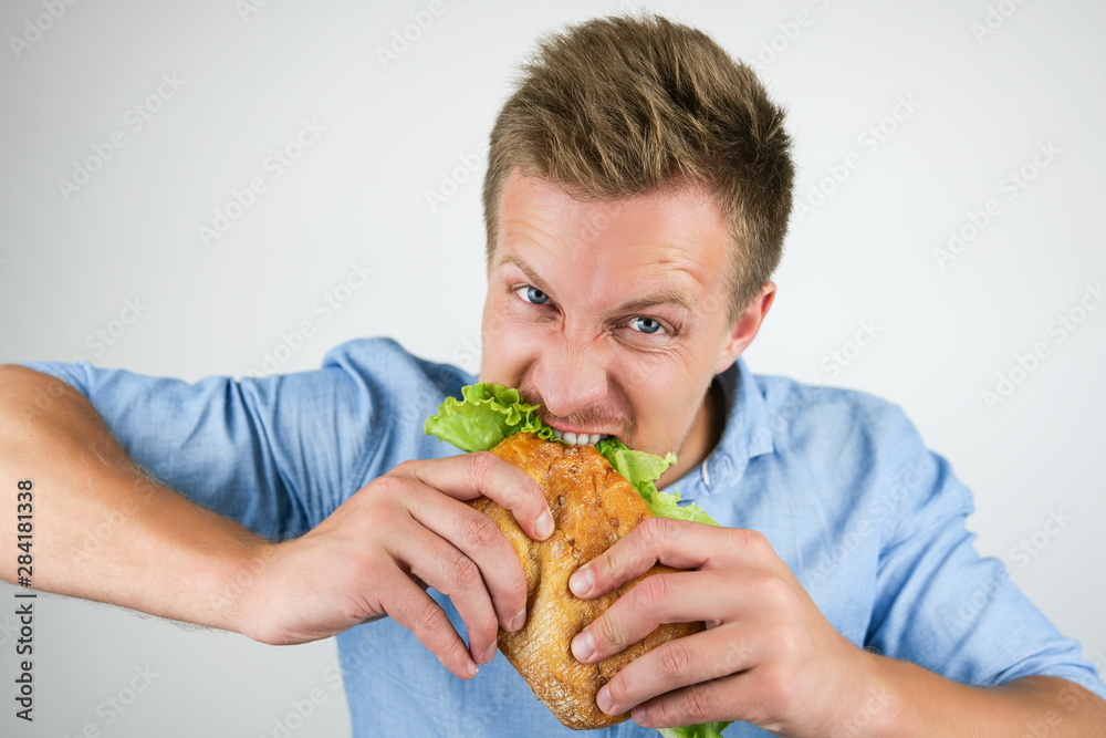 young handsome hungry man biting fresh sandwich with salad leaf on isolated white background