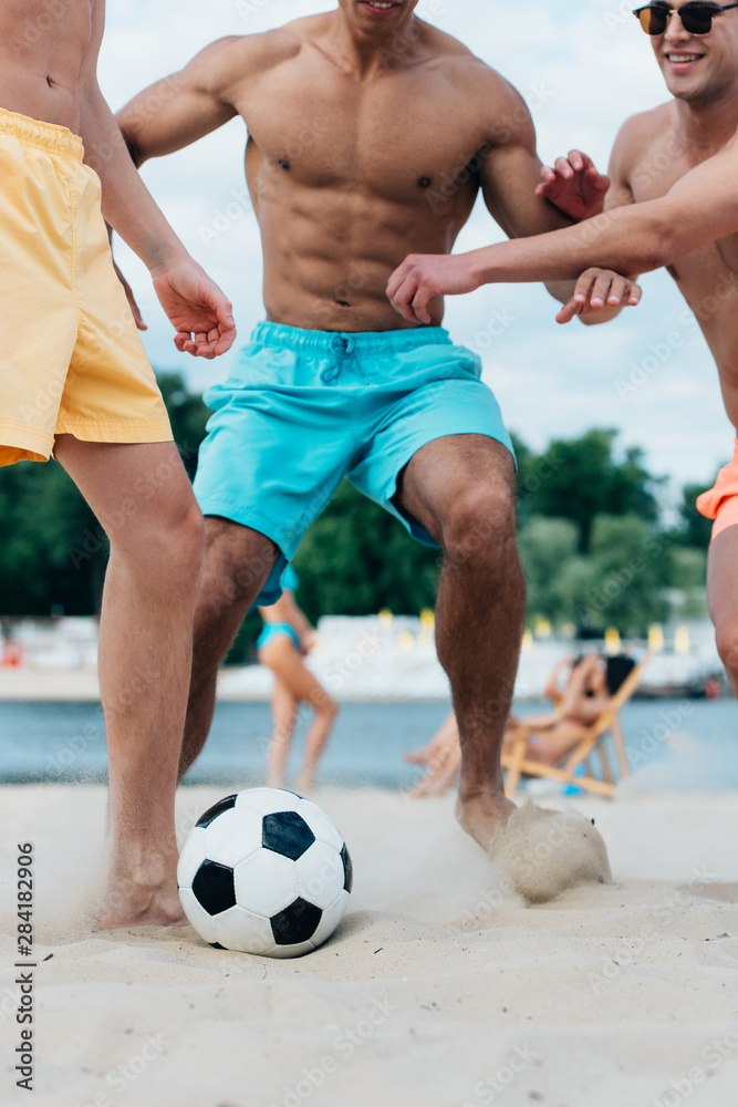 partial view of young multicultural friends playing football on beach