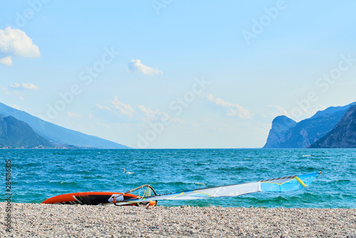 Windsurfing board lying on an empty pebble beach by the lake Garda (Lago di Garda), Italy
