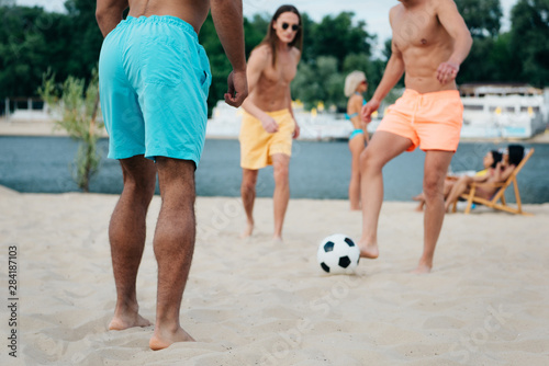 cropped view of young multicultural friends playing football on beach
