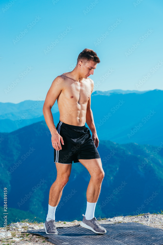 Shirtless bodybuilder enjoying the amazing lake view from the top of the mountain on a summer day.