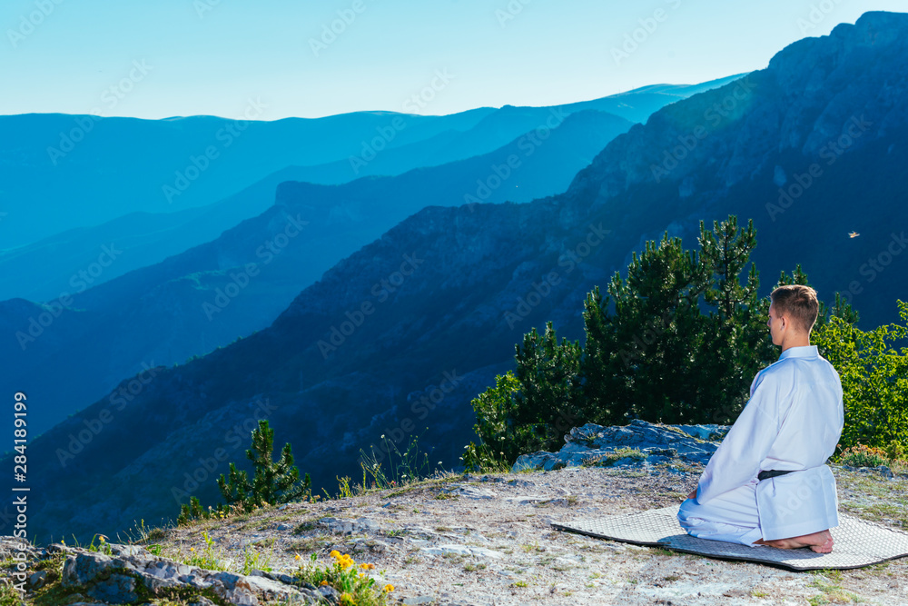 Karate master meditating on top of a mountain wearing kimono while looking down at the mountain lake.