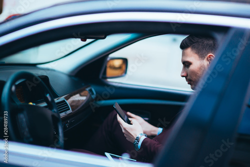 Young businessman looking at his cellphone while comfortably sitting at the front seat in his luxury limo. © qunica.com