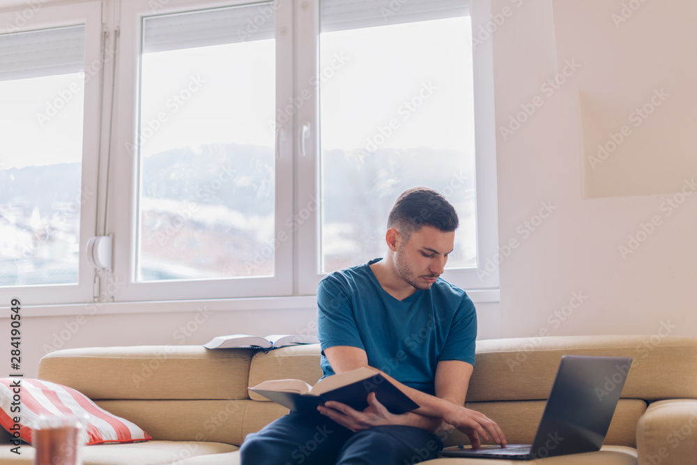 Handsome student studying on the couch with few opened books and a laptop next to him. Handsome student studying on the couch with few opened books and a laptop next to him.