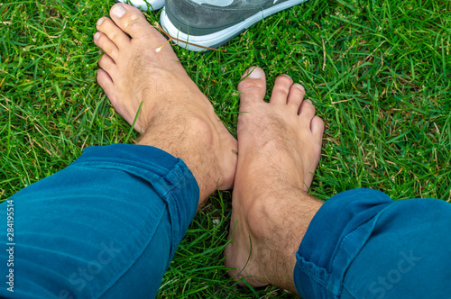 Man takes off sneakers and rests barefoot on green lawn. Blur backgroun photo