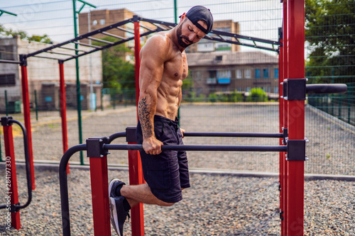 Strong muscular man doing push-ups on uneven bars in outdoor street gym. Workout lifestyle concept. © zamuruev