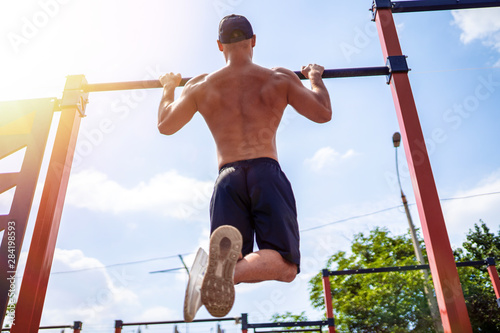 Brutal athletic man making pull-up exercises on a crossbar at outdoor streeet gym. Back view. photo