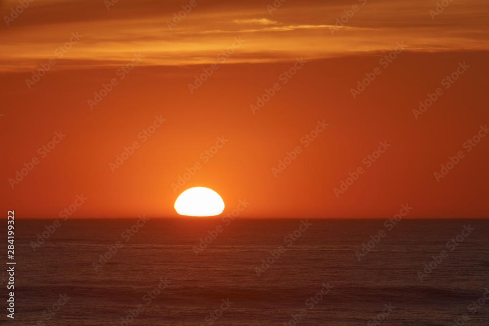    Red-violet sunset over the Atlantic ocean. White disc of the sun over the red sea at sunset. Natural bright background is suitable for postcard, touristic guide, greeting card.