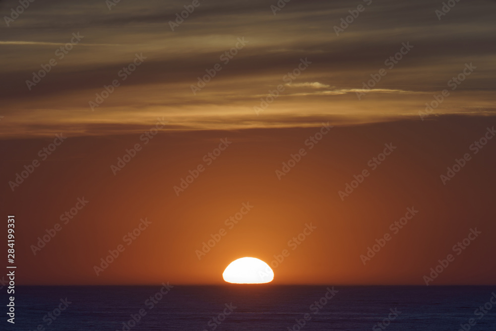    Red-violet sunset over the Atlantic ocean. White disc of the sun over the red sea at sunset. Natural bright background is suitable for postcard, touristic guide, greeting card.