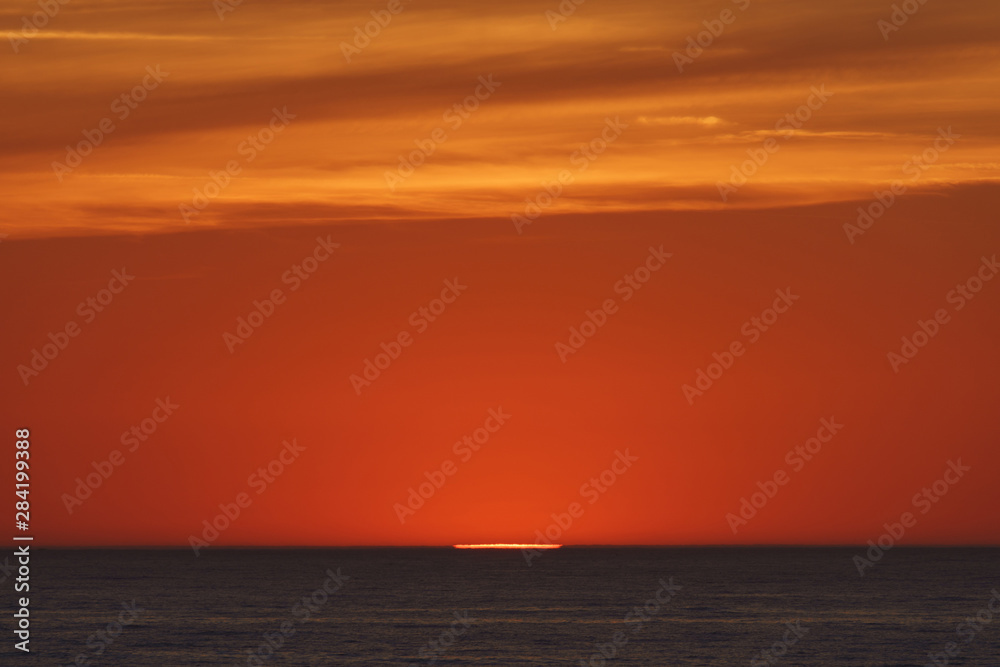    Red-violet sunset over the Atlantic ocean. White disc of the sun over the red sea at sunset. Natural bright background is suitable for postcard, touristic guide, greeting card.