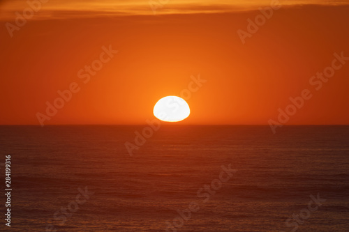 Fototapeta Naklejka Na Ścianę i Meble -     Red-violet sunset over the Atlantic ocean. White disc of the sun over the red sea at sunset. Natural bright background is suitable for postcard, touristic guide, greeting card.