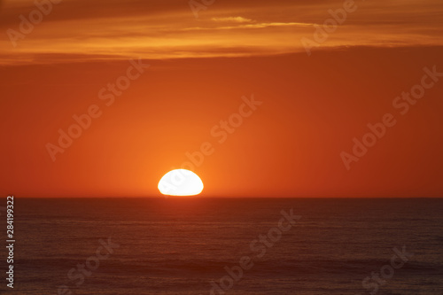  Red-violet sunset over the Atlantic ocean. White disc of the sun over the red sea at sunset. Natural bright background is suitable for postcard, touristic guide, greeting card.