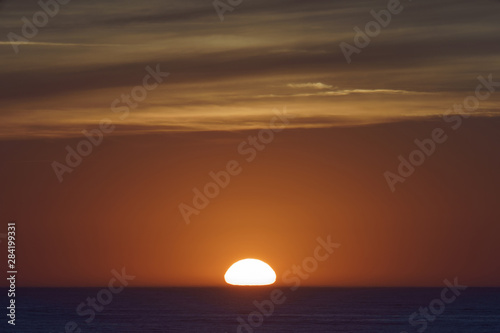  Red-violet sunset over the Atlantic ocean. White disc of the sun over the red sea at sunset. Natural bright background is suitable for postcard, touristic guide, greeting card. © Yury and Tanya