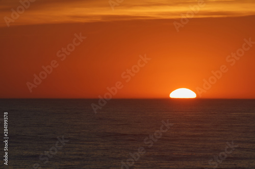    Red-violet sunset over the Atlantic ocean. White disc of the sun over the red sea at sunset. Natural bright background is suitable for postcard, touristic guide, greeting card. © Yury and Tanya