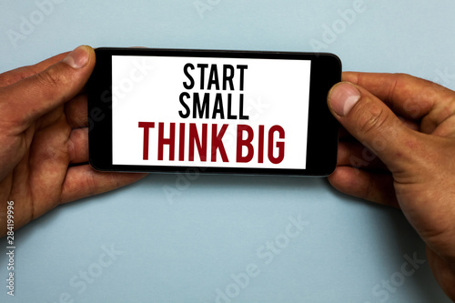 Word writing text Start Small Think Big. Business concept for Initiate with few things have something great in mind Human hand hold smartphone with red and black letters on shadow blue floor