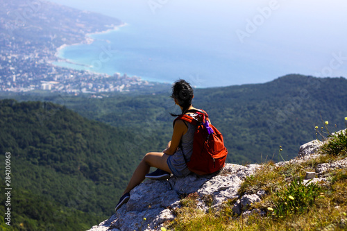 A young traveler girl sits on top of the Crimean mountain Ai-Petri and enjoys the beauty of the sea landscape.