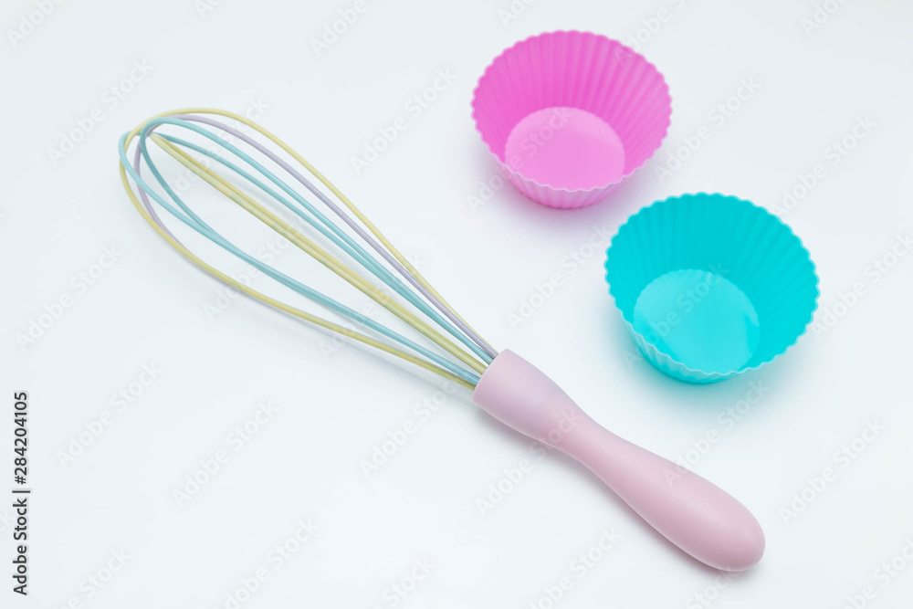 Set of kitchen accessories for baking: silicone moulds for cupcakes of pink and blue colors and a crown for stirring ingradients. White Background Set of kitchen accessories for baking: silicone moulds for cupcakes of pink and blue colors and a crown for stirring ingradients. White Background