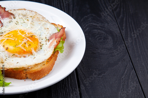 Close up view on grilled toast with bacon and egg on white plate on dark wooden background. Copy space. Food phoro for breakfast. Top view photo
