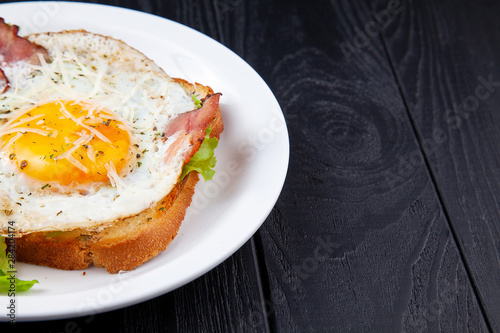 Close up view on grilled toast with bacon and egg on white plate on dark wooden background. Copy space. Food phoro for breakfast. Top view