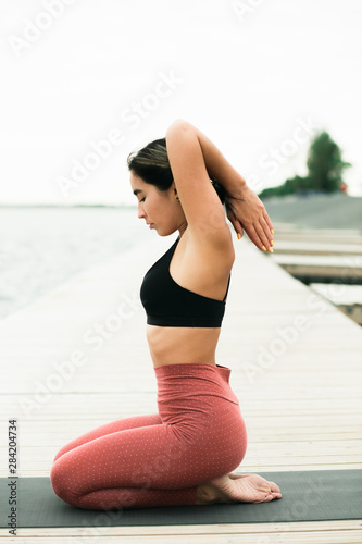 Asian attractive young girl doing yoga outdoors on the pier by the lake.