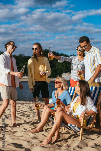 cheerful multicultural friends talking while drinking beer on beach © LIGHTFIELD STUDIOS