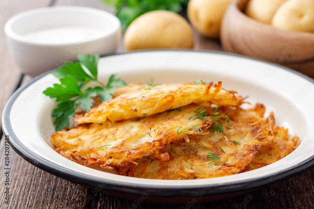 Potato pancakes or latkes or draniki in plate on dark wooden table. Selective focus. Potato pancakes or latkes or draniki in plate on dark wooden table. Selective focus.