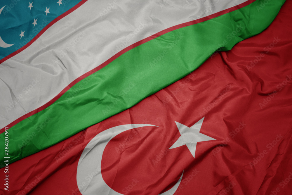 waving colorful flag of turkey and national flag of uzbekistan.