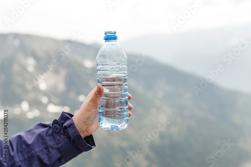 Female tourist holding bottle of clear water. Mountains landscape. Hand holding plastic bottle. Say no to plastic. Save the world.