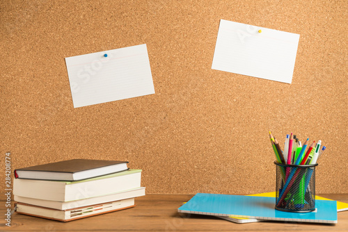 Books, notebooks and school supplies on wooden boards with a cork board in the background.