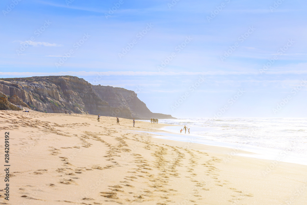 People relaxing and walking on the ocean beach in a shine bright light at sunny day. Wonderful romantic seascape of ocean coastline. People relaxing and walking on the ocean beach in a shine bright light at sunny day. Wonderful romantic seascape of ocean coastline.