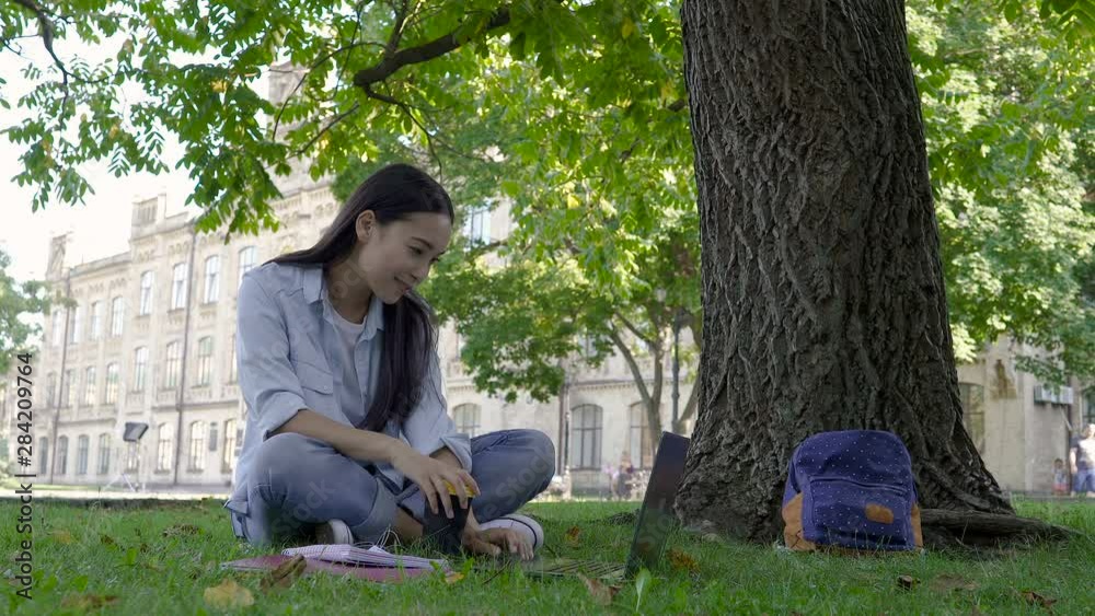 Asian student girl studying in the park. Sitting on the lawn, working with notebook. Asian student girl studying in the park. Sitting on the lawn, working with notebook.