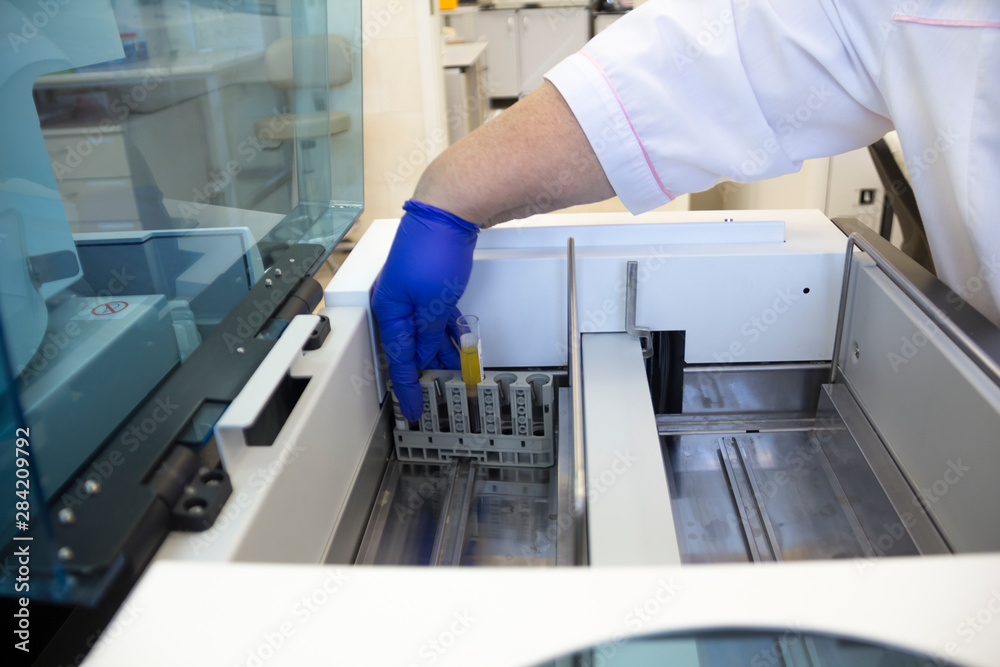 biochemical laboratory equipment. blood test apparatus. Laboratory biochemistry analyzer. a lab technician's hand in a blue latex glove puts a blood tube in a blood test apparatus biochemical laboratory equipment. blood test apparatus. Laboratory biochemistry analyzer. a lab technician's hand in a blue latex glove puts a blood tube in a blood test apparatus