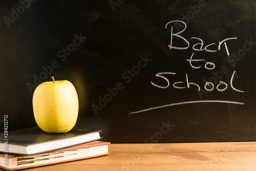 An apple and some books on wooden boards with a blackboard in the background.