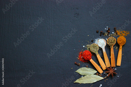 Various spices (ground turmeric pepper ginger cinnamon herb seasoning salt paprika cumin)in wooden vintage spoons on the black table. The view from the top. Copy space.