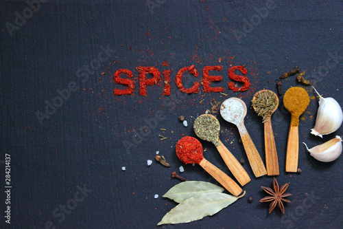 The word spice is written on a black background. Various spices ground turmeric pepper ginger cinnamon herb seasoning salt paprika cumin wooden vintage spoon on black table. The view from the top. Spi