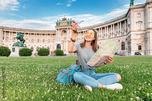 Happy asian woman traveler with map sitting on a green lawn in Vienna city. Tourism and vacation in Europe concept