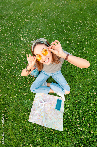 Happy asian woman sitting on grass in park with open map and smartphone and airplane toy. Tourism and travel concept
