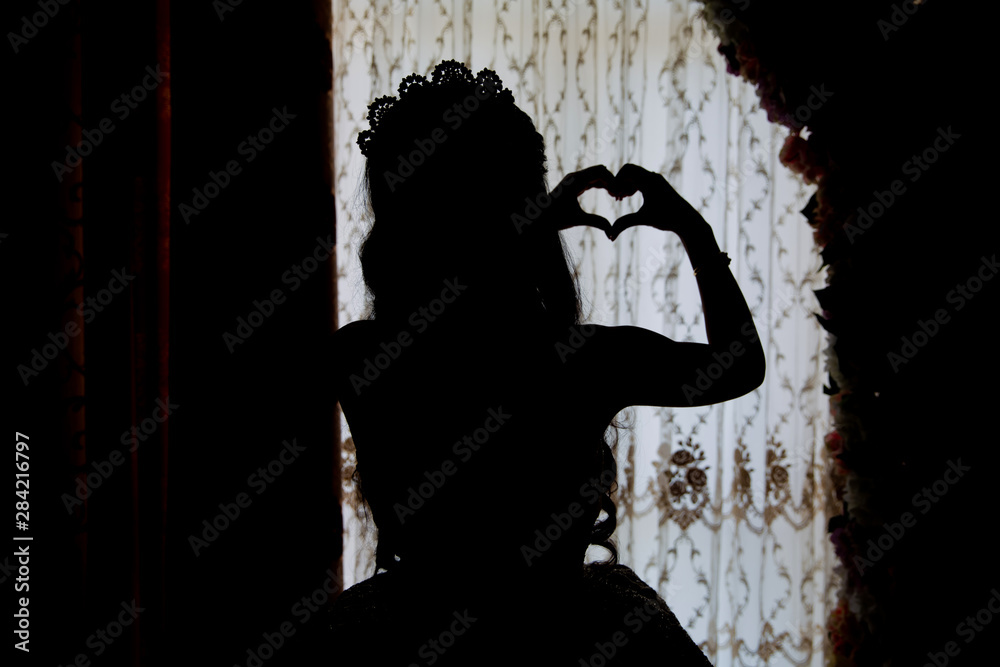 The bride looks out of the huge window in the bridal suite revealing the backside of the wedding dress . The back side of a white wedding dholds a heart in his handress. The bride looks out of the huge window in the bridal suite revealing the backside of the wedding dress . The back side of a white wedding dholds a heart in his handress.