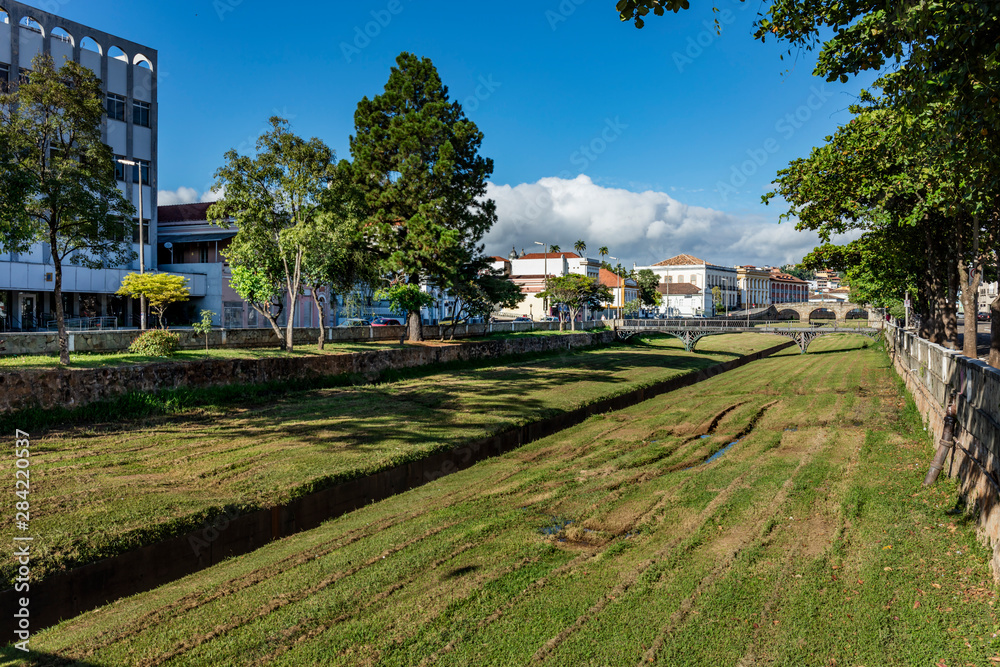 Fototapeta premium River with green grass and old buildings of the city hall of the historical and tourist city of Sao Joao del Rey, in the state of Minas Gerais, Brazil.