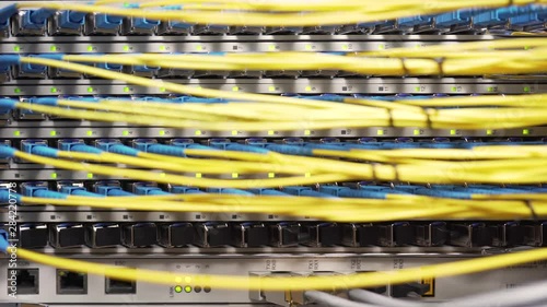 Sliding close-up shot of an optical fiber connector board with yellow cables coming out of it and blinking green lights photo