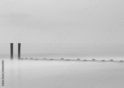 BnW photo of Lonely pier in the ocean at sunrise with long exposure 