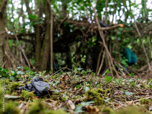 Plastic bag in a forest in focus, Handmade hut in the background out of focus. Concept ecology in natural environment.