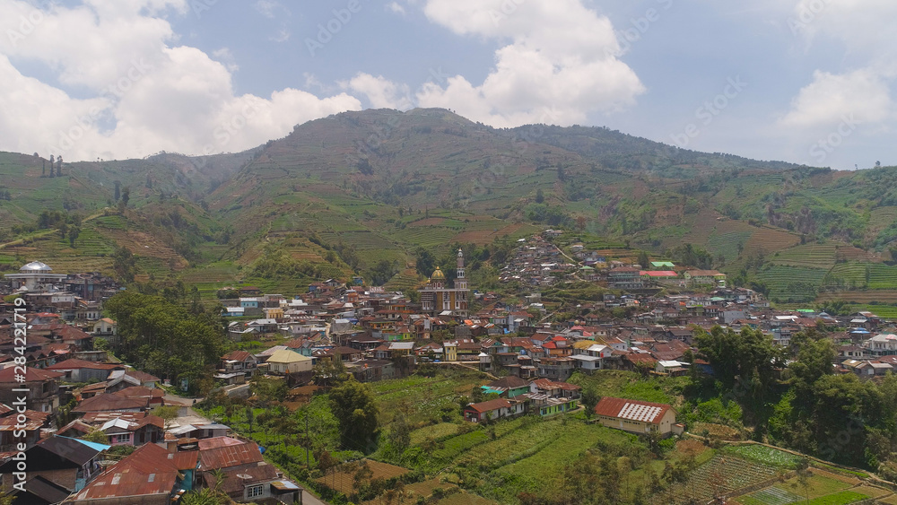 asian town with mosque in mountains among agricultural land, rice terraces. mountains with farmlands, rice fields, village, fields with crops, trees. Aerial view farm lands on mountainside. tropical