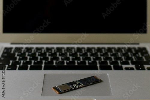 SSD drive diagonally on the trackpad. The laptop takes up the entire frame horizontally. Half screen. Keyboard blurred. Photo in neutral color.