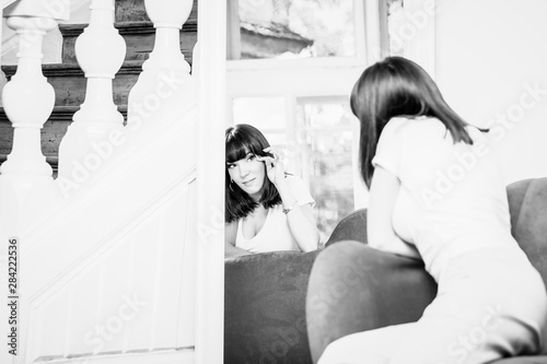 Beautiful young woman looking at her reflection in a mirror. Black and white photo