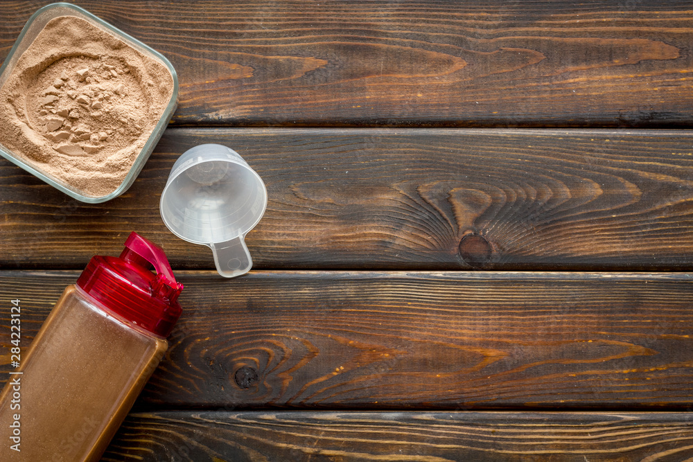 Protein powder and shaker for sport diet on wooden background top view copyspace
