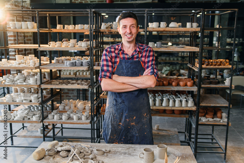 Attractive male potter with crossing hands looking to camera in the pottery. Attractive male potter with crossing hands looking to camera in the pottery.